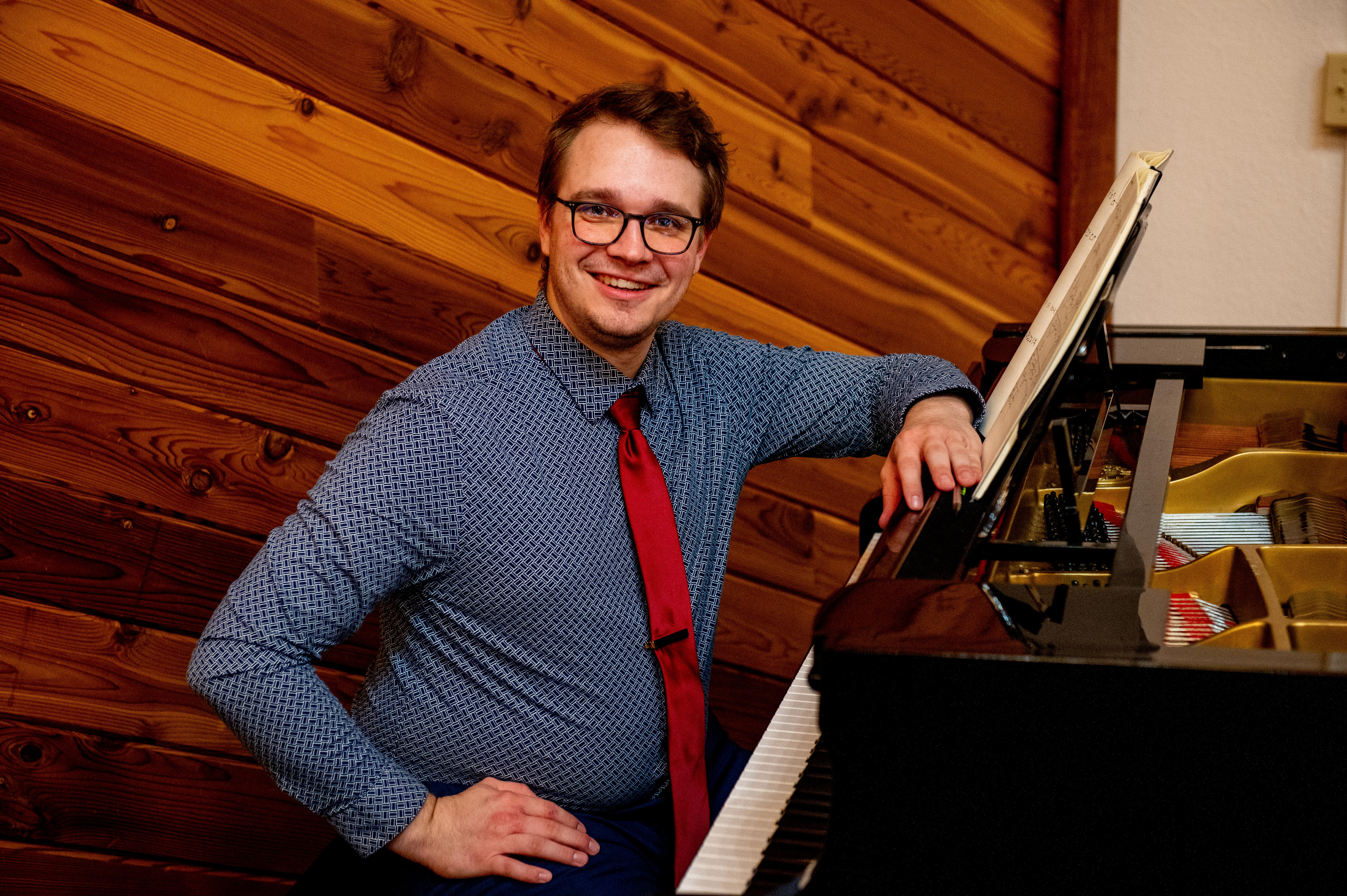 Composer Matthew Compton sits at a piano, smiling, ready to write a new work for handbells for Bells of the Cascades in honor of their 35th anniversary.