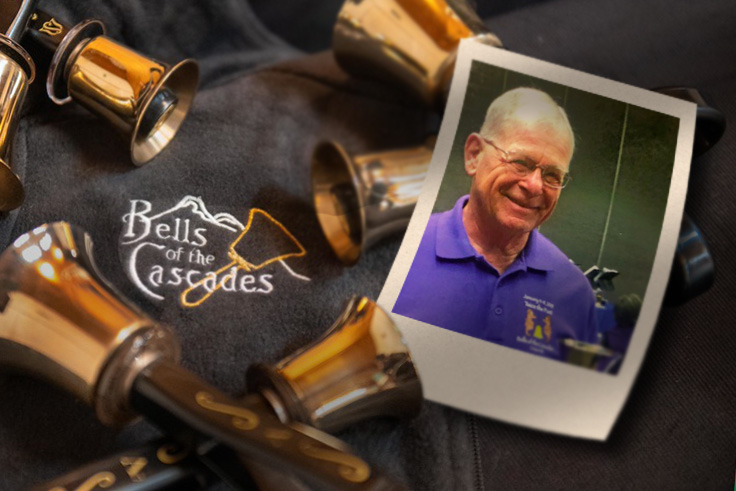 A photograph of Dave Schade rests beside handbells on a table including an embroidered version of the Bells of the Cascades logo.