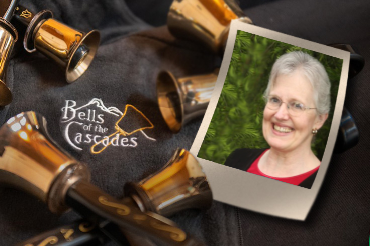 A photograph of Nancy Hascall rests beside handbells on a table including an embroidered version of the Bells of the Cascades logo.